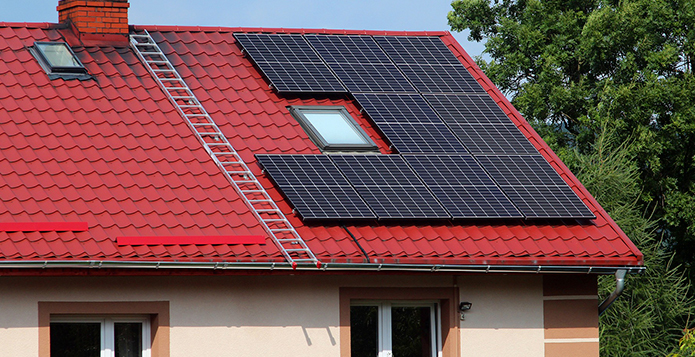Tejado de casa con paneles solares instalados sobre un techo rojo inclinado, rodeado de árboles. Sistema de almacenamiento de energía solar en Las Palmas.